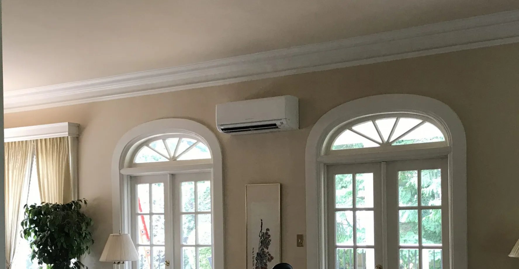 White mini-split unit mounted on interior wall between arched windows