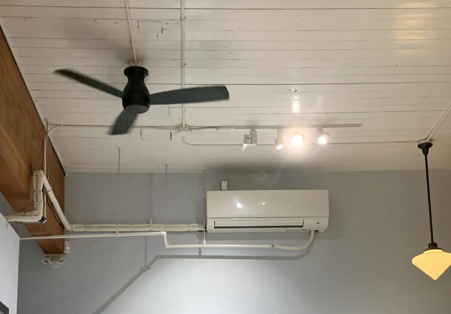 White mini-split air conditioning unit mounted on wall with ceiling fan in commercial kitchen space