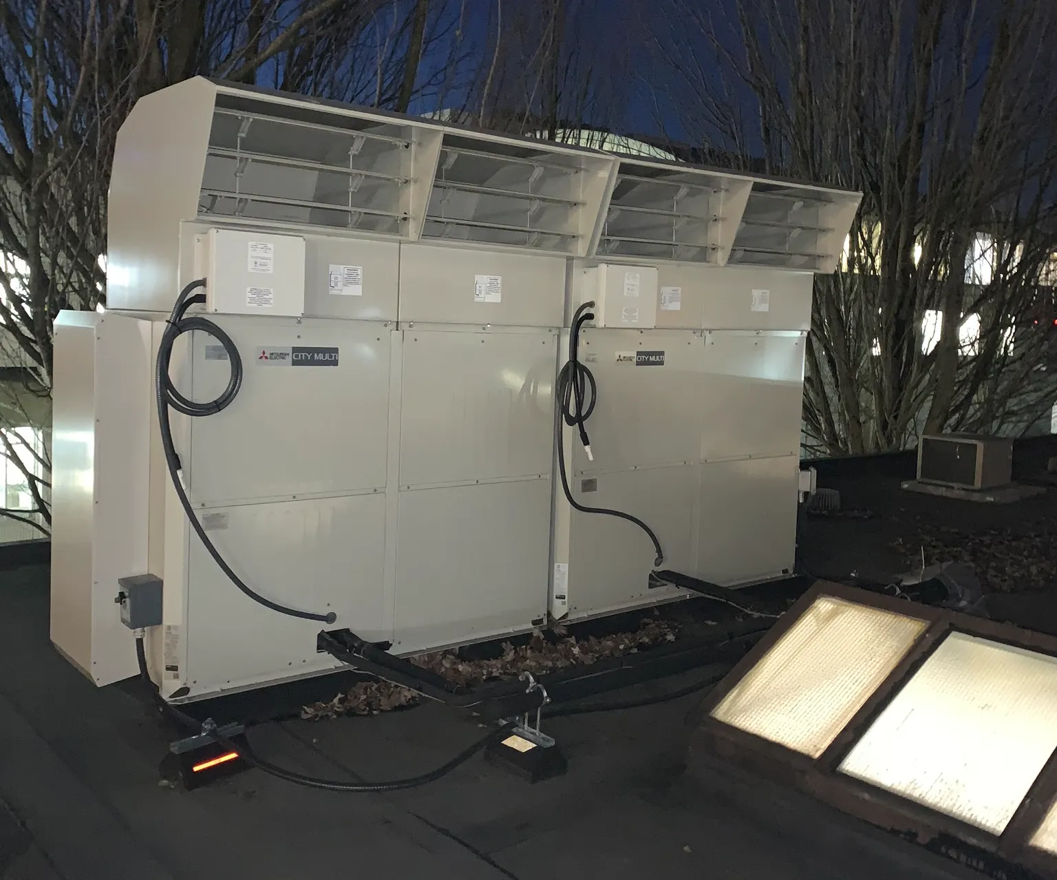 Multiple Mitsubishi outdoor condenser units installed on commercial building rooftop at night